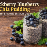 A pair of mason jars with blackberry blueberry chia pudding, topped with fresh blackberries, blueberries, and mint, placed on a rustic wooden table.